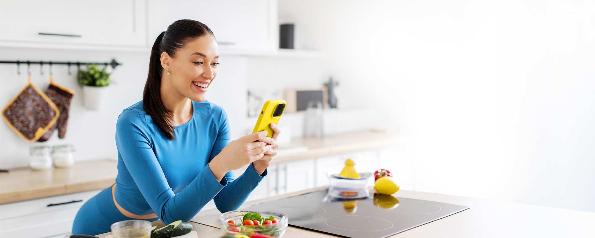 Woman smiling in a kitchen while using the Portions Master app with fresh vegetables on the counter.