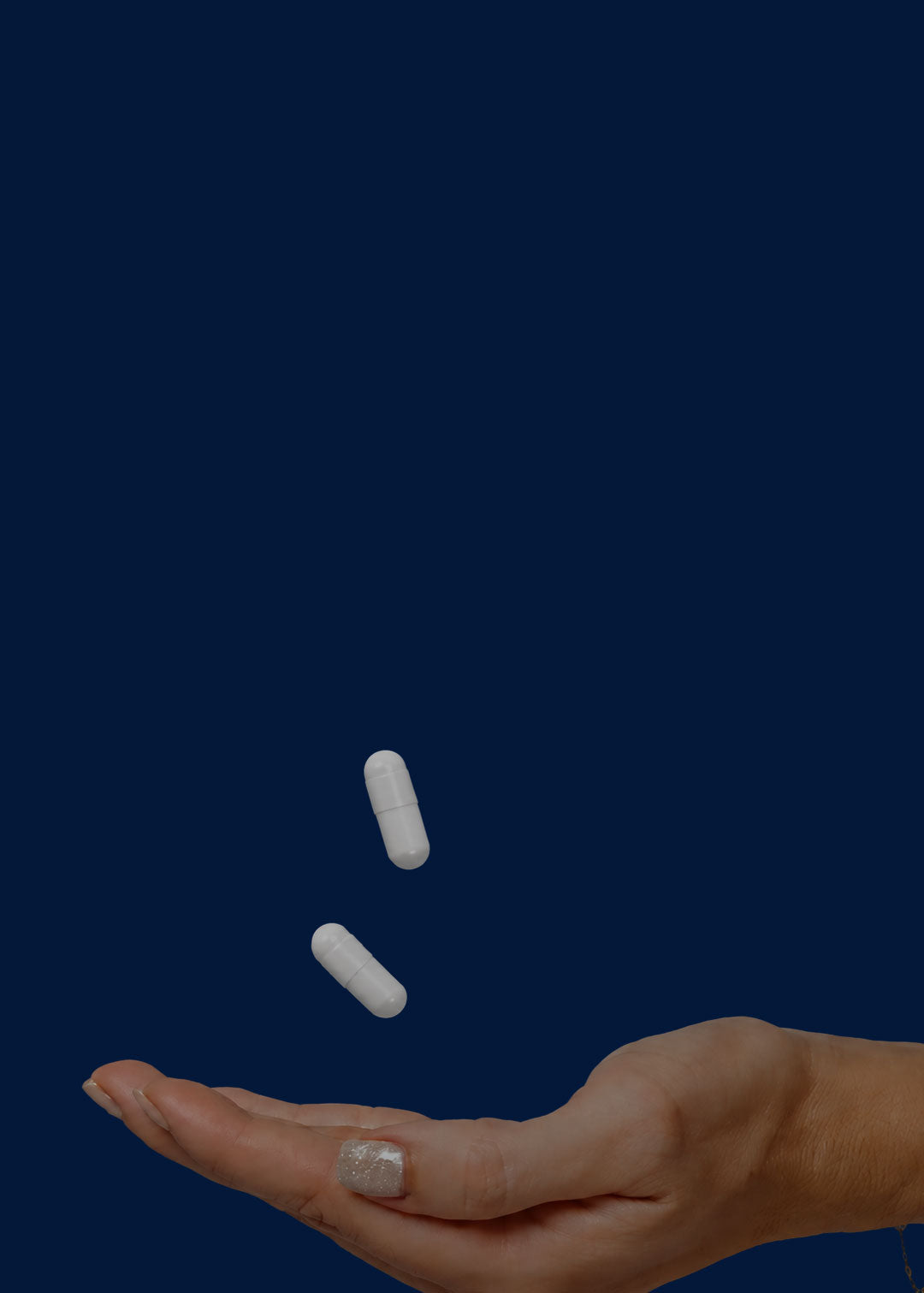 Hand catching two supplement capsules against a solid blue background